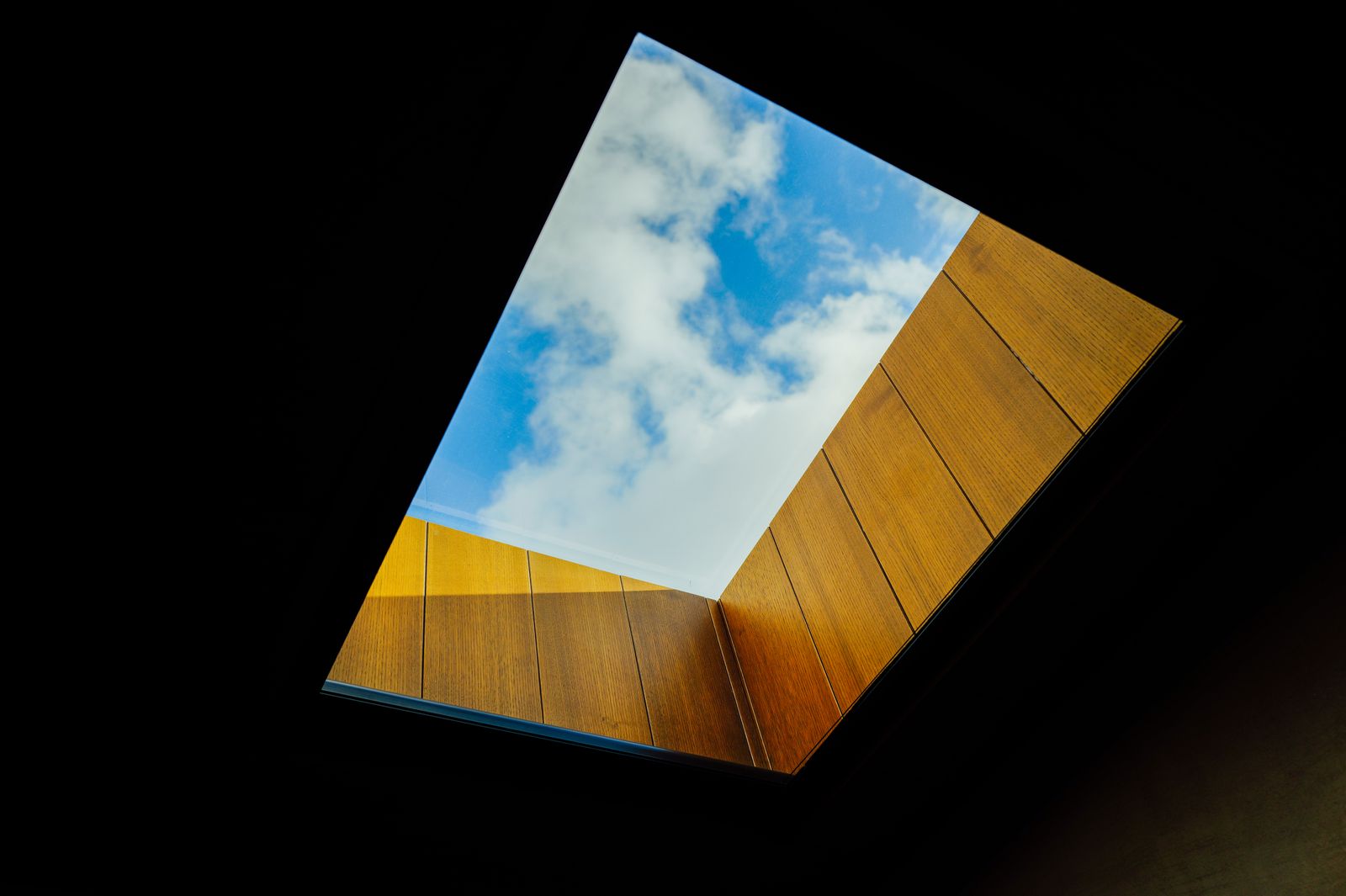 A modern skylight reveals a bright blue sky with passing clouds, framed by wooden paneling.