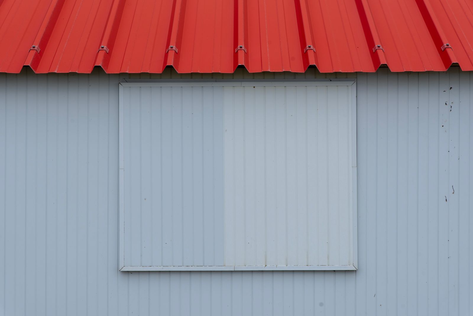 Minimalist image of a red metal roof with blue-grey corrugated panel wall.
